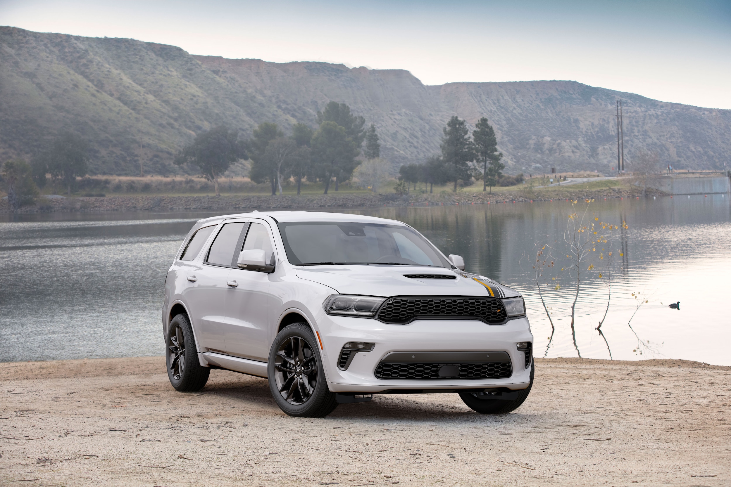 A white Dodge Durango parked at the edge of a Colorado lake with foothills in the background