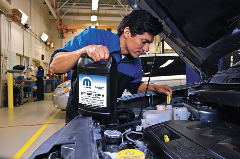 A Mopar-certified technician adding coolant while servicing a vehicle in the shop